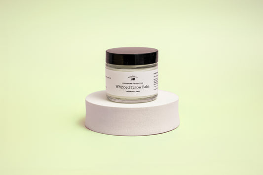 Jar of whipped balm on a white pedestal against a light green background