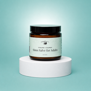 Elderberry Co. Cooling + Calming Sinus Salve for Adults in a 4 oz amber glass jar, shown on a white display pedestal with a soft blue background.