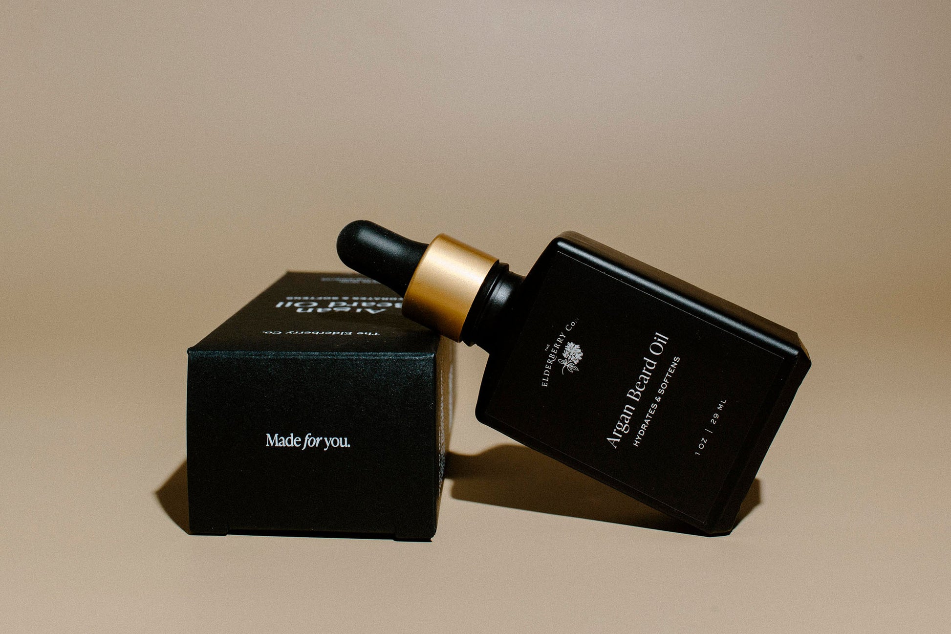 Elderberry Co. Argan Beard Oil bottle resting on its product box, showcasing a premium beard oil formulated to hydrate, soften, and nourish facial hair.