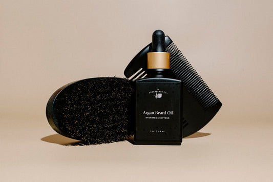 Black beard oil bottle with a comb and brush on a beige background