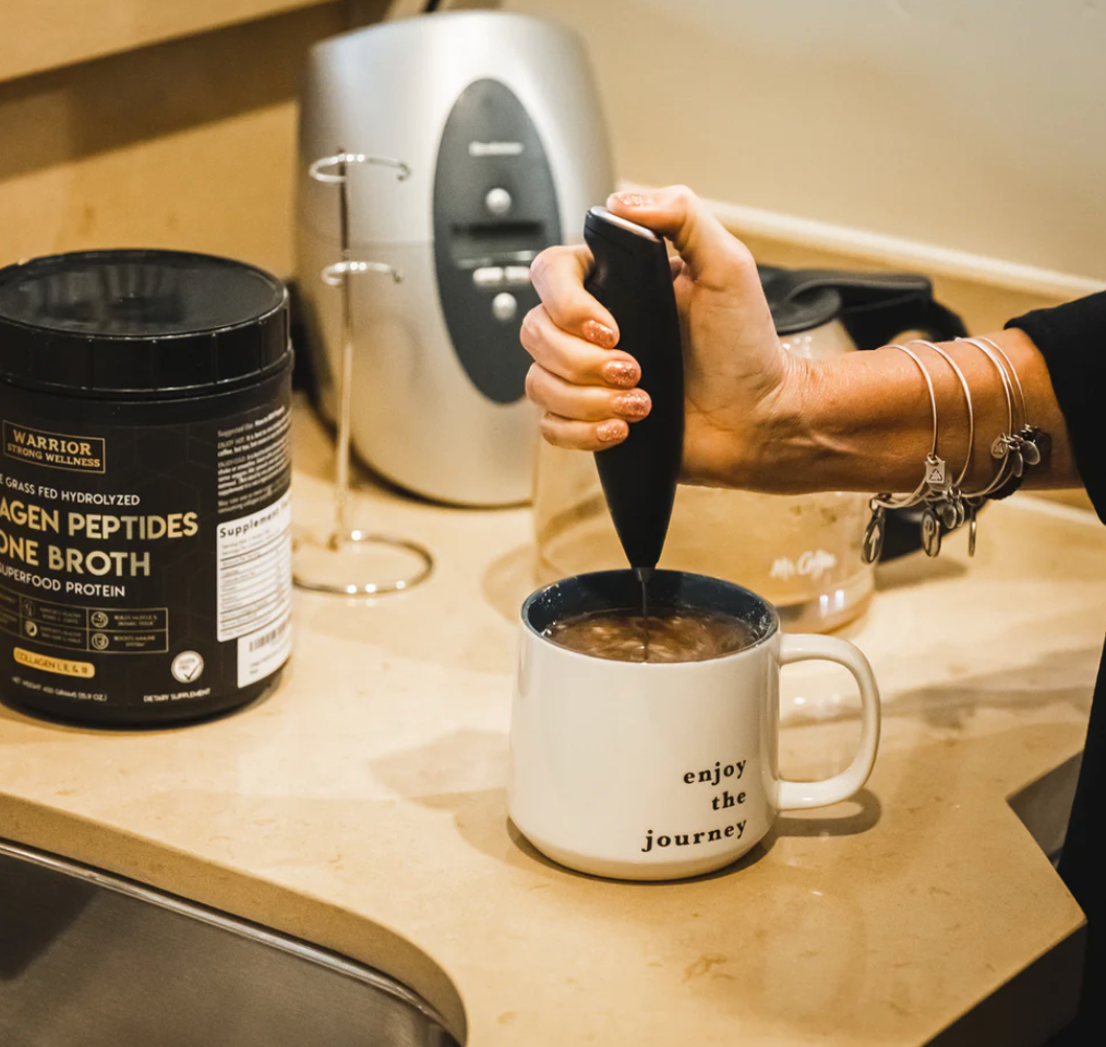 Handheld milk frother blending collagen powder into coffee beside Warrior Strong Wellness Collagen Peptides & Bone Broth, demonstrating easy mixing for drinks and recipes.