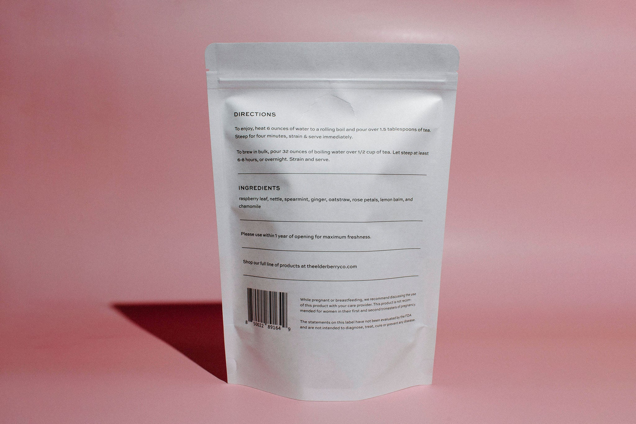 A stand-up pouch of Elderberry Co. Raspberry Tea back on a solid pink background.