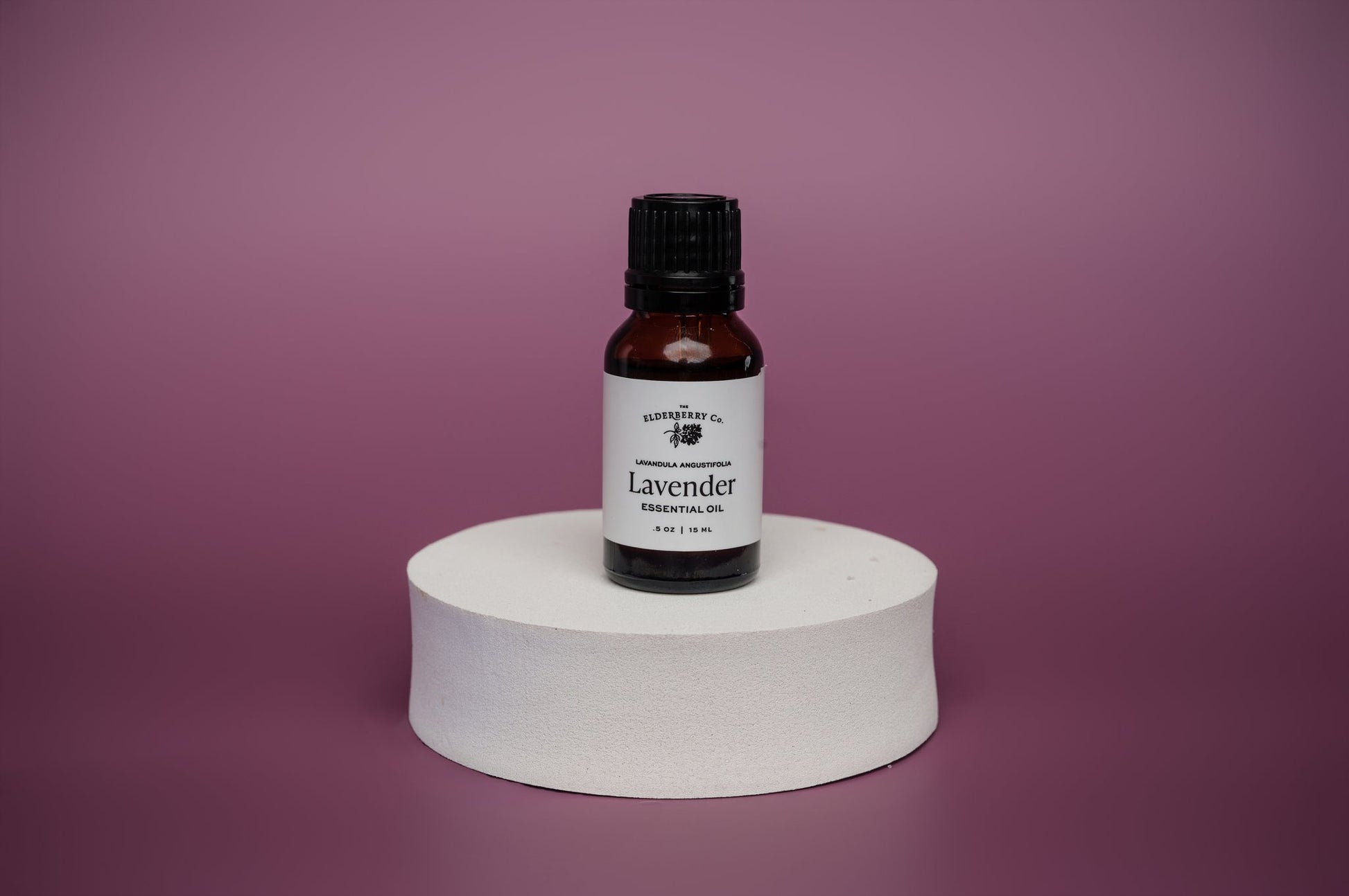 Bottle of lavender essential oil on a white pedestal against a purple background