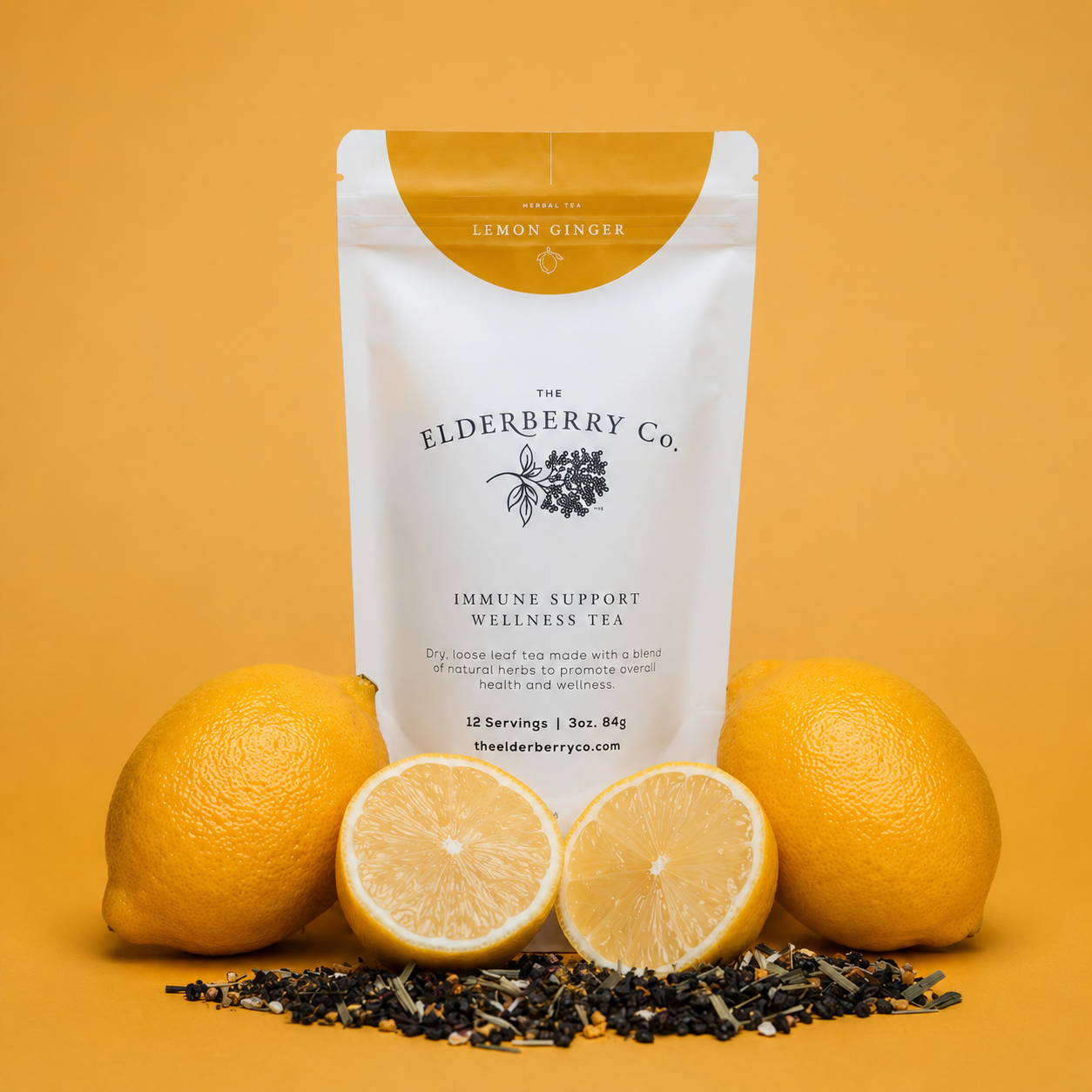 A stand-up pouch of The Elderberry Co. Lemon Ginger Immune Support Wellness Tea, styled with whole and sliced lemons and loose leaf tea on a solid warm yellow background.