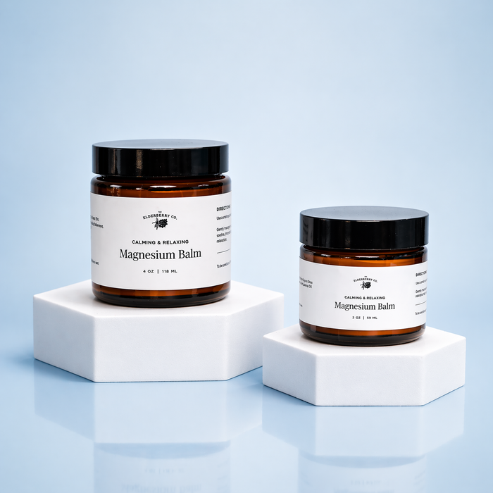Two jars of magnesium balm on white stands against a light blue background