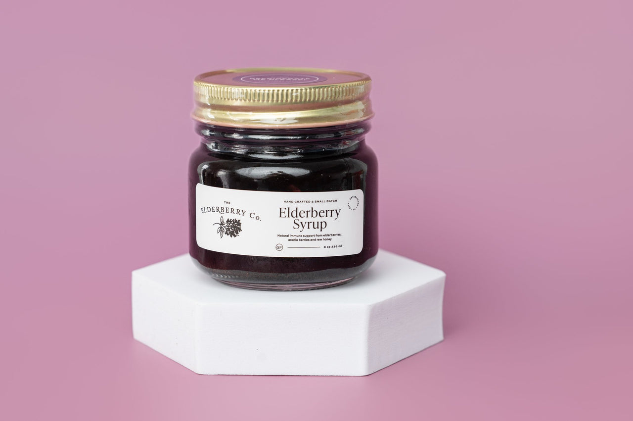 Jar of elderberry syrup on a white stand with a pink background