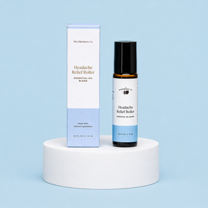 The Elderberry Co. Headache Relief Roller essential oil blend with its matching retail box displayed on a white pedestal against a soft blue background.