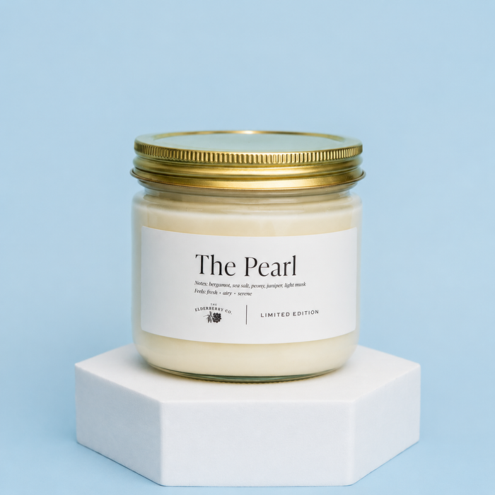 Candle jar labeled 'The Pearl' on a white platform with a light blue background