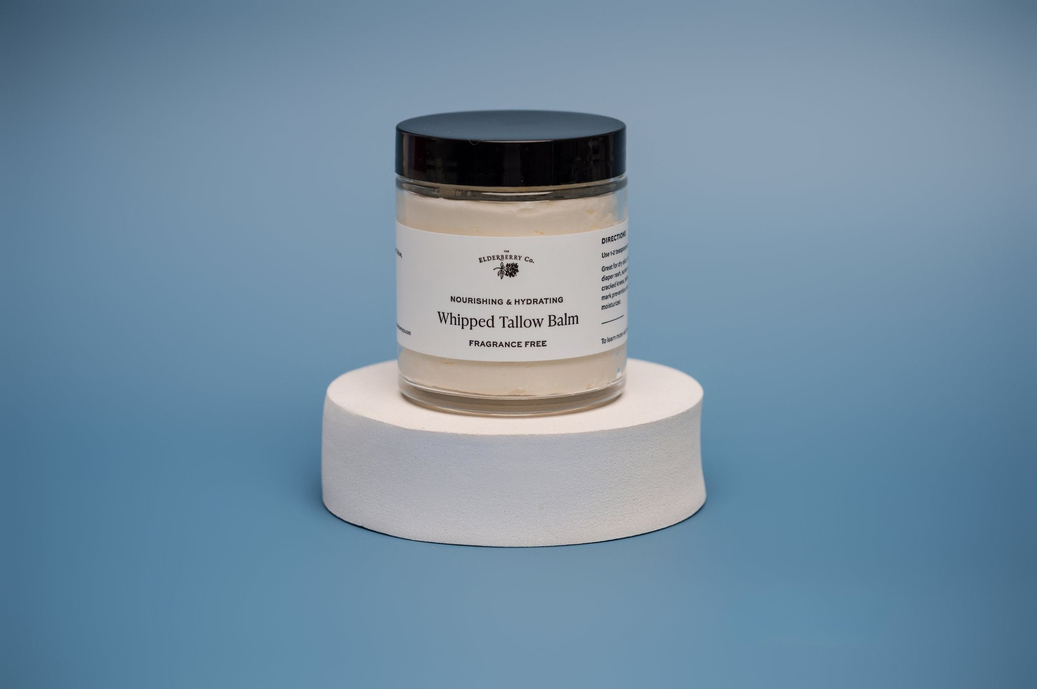 Three jars of Fragrance Free Whipped Tallow Balm, with one jar open showing the creamy product inside. The jars are placed on a white surface with a blue background.