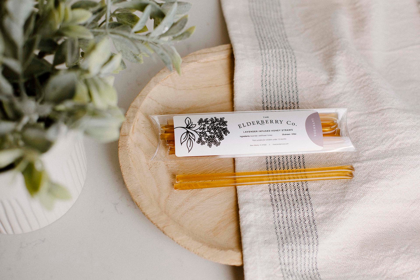 Elderberry Co. Lavender Honey Infused Straws displayed on a wooden tray with a linen towel, featuring individually wrapped honey straws in a cozy lifestyle setting.